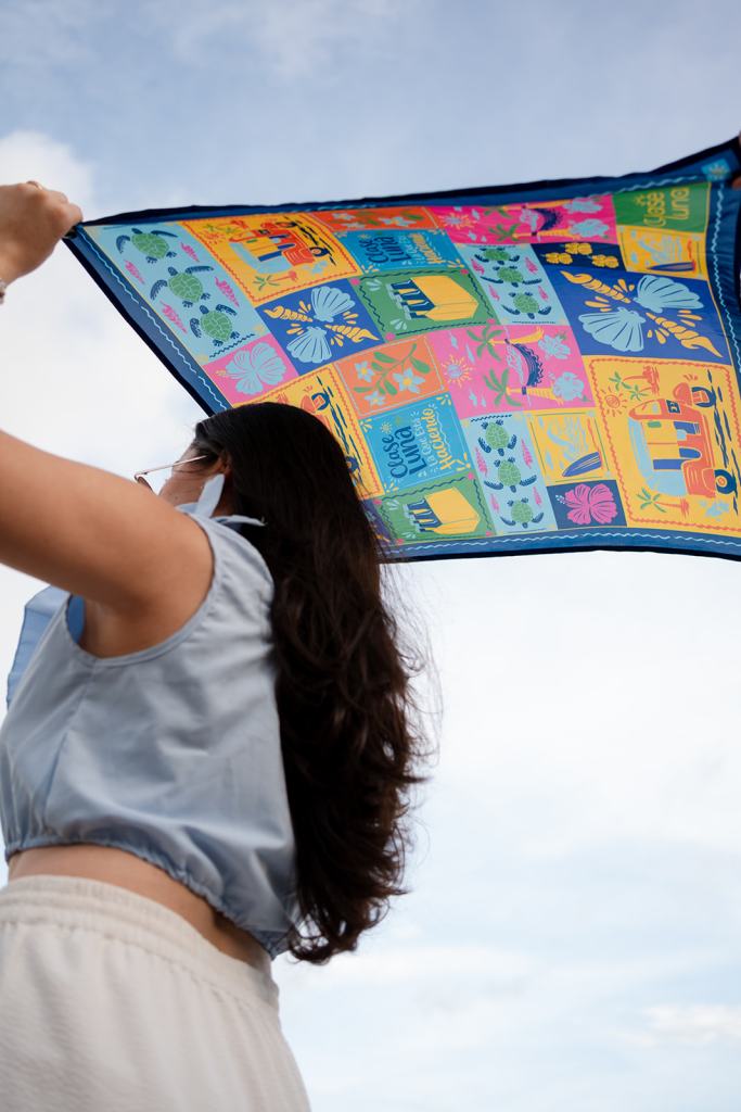 Modelo sosteniendo al viento un pañuelo estampado de Clase Luna, sesión de fotos en la playa